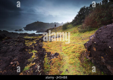 Una persona che guarda come un oscuro moody tempesta si muove oltre la costa frastagliata che la circonda. Foto Stock