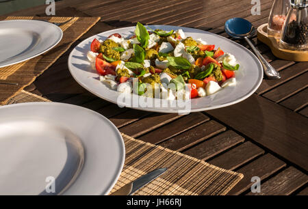 Insalata caprese con pesto e freddo patate bollite, servita su bianco stoviglie, sul patio con giardino tavolo in estate il sole, Scotland, Regno Unito Foto Stock