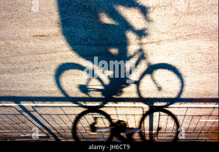 Sfocata ciclista silhouette e ombra su un protetto percorso in bicicletta nel tramonto capovolto Foto Stock