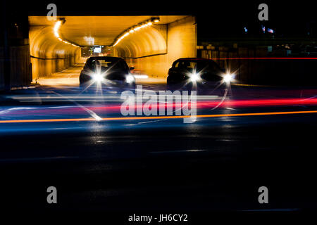 Il traffico di notte sulle strade della città. Vetture accodate all'uscita del tunnel in attesa presso l'intersezione durante la guida di veicoli che si spostano oltre lasciando colore sentieri di luce Foto Stock
