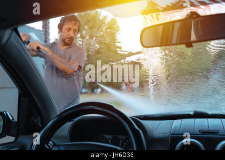 Uomo auto lavaggio in self-service car wash stazione, visto dall'interno del veicolo, il fuoco selettivo Foto Stock