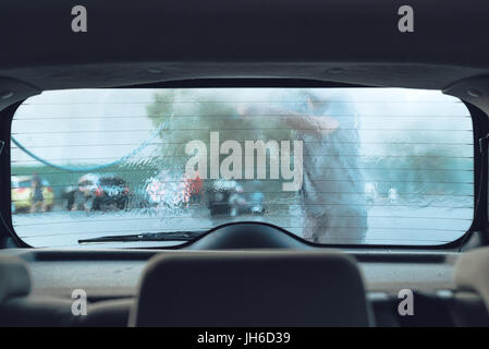 Uomo auto lavaggio in self-service car wash stazione, visto dall'interno del veicolo, il fuoco selettivo Foto Stock