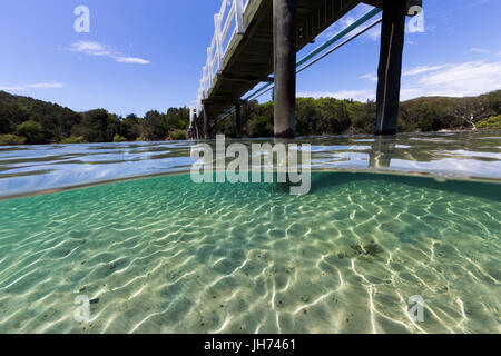 Un ponte attraversa belle acque incontaminate in un giorno di estate in questo underwater immagine sdoppiata. Foto Stock