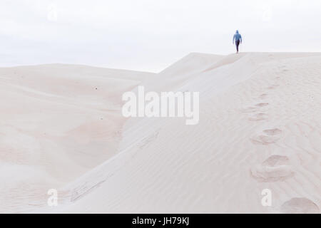 Una persona che cammina lungo una duna di sabbia ridge lasciando dietro di sé una scia di orme nella sabbia. Foto Stock