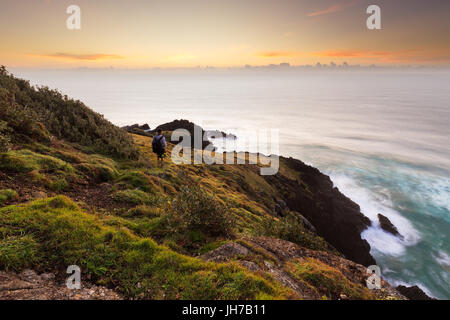 Una persona si erge su un promontorio sopra una rupe a guardare un bel tramonto sull'oceano. Foto Stock