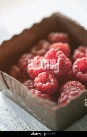 Lamponi close-up in una scatola marrone su uno sfondo luminoso. Il telaio orizzontale. Foto Stock