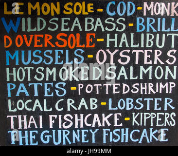 Il segno e la lavagna al di fuori di un pesce fresco shop che mostra le diverse varietà di pesce e frutti di mare a disposizione per la vendita. Foto Stock