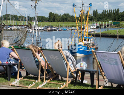 Greetsiel, Germania. 13 Luglio, 2017. La taglierina di granchio ·i fratelli· giacente al di ancoraggio nel porto di Greetsiel, Germania, 13 luglio 2017. I vacanzieri possono essere visti in primo piano giacente su sedie a sdraio sulla spiaggia. Una pressione elevata ridge è il tempo per una piacevole giornata in Germania settentrionale. Foto: Ingo Wagner/dpa/Alamy Live News Foto Stock