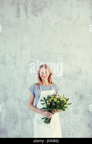 Ritratto di un fioraio con bouquet vicino al muro grigio Foto Stock