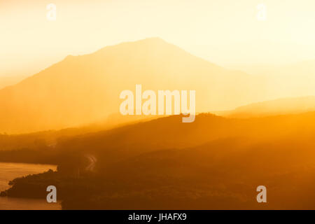 Un avvolgimento highway road scompare in strati di montagna e un tramonto dorato. Foto Stock