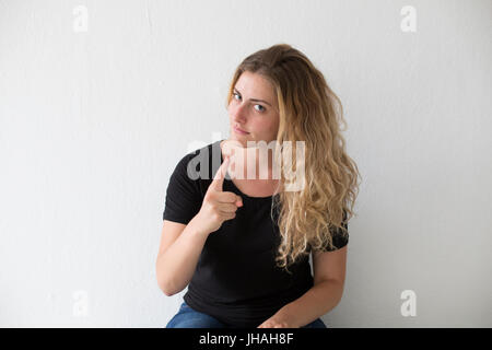 Giovani, bionda, donna caucasica esprime emozioni negative, ira, urlando e puntare il dito al visualizzatore e fotografo su uno sfondo bianco. Foto Stock