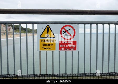 Un segno Attenzione gente di mare poco profondo e acqua e dire alla gente di non tuffarsi o salta fuori il molo (Boscombe pier vicino a Bournemouth in Dorset, Inghilterra). Foto Stock