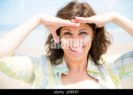 Funny donna di mezza età l'applicazione di crema di protezione solare sulla faccia sulla spiaggia Foto Stock