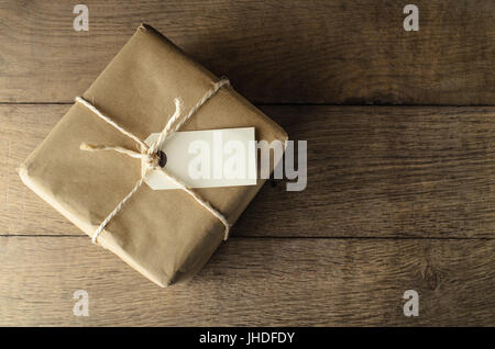 Una forma quadrata parcel, avvolto in carta marrone e legati con spago. Etichetta vuota tag e il legno di quercia tavolato di fornire copia di spazio. Foto Stock
