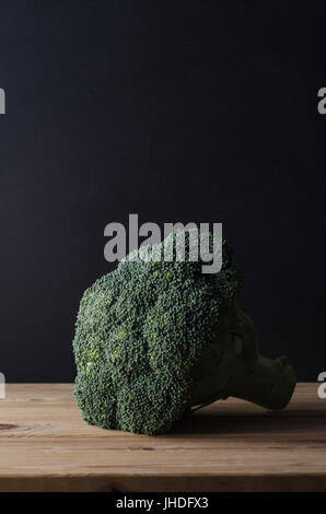 Una testa di colore verde scuro con broccoli peduncolo intatto, su legno tabella planked contro la lavagna nera dello sfondo. Moody illuminazione. Foto Stock