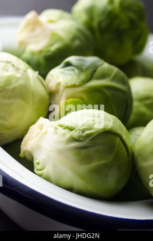 Close up i cavoletti di Bruxelles ammucchiati in uno smalto bianco teglia. Foto Stock