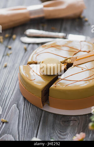 Panificio con un pezzo di un insolito giallo torta mousse con mandorle dacquoise, confit di lampone, strato croccante con nocciole caramellate e polvere di lampone, mousse sulla base di cioccolata amara servita su un tavolo di legno Foto Stock