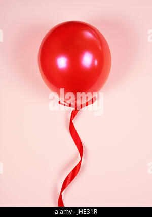 Il palloncino rosso su un nastro rosso su uno sfondo rosa Foto Stock