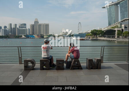 25.05.2017, Singapore, Repubblica di Singapore, in Asia - i turisti siedono lungo il Fiume Singapore a Marina Bay e guardare il Singapore Flyer. Foto Stock