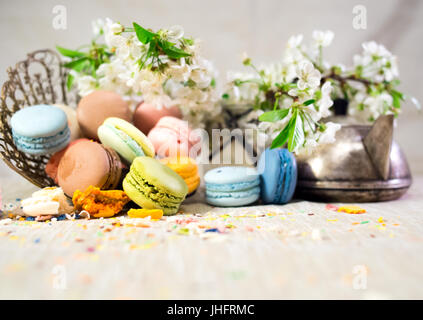 Amaretti multicolore su una tabella con vaso orientale e il ramo di ciliegio in fiore Foto Stock