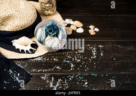 Cappello di paglia con amaretti blu e sale marino con conchiglie sullo sfondo di legno Foto Stock