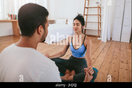 Bella giovane donna fare yoga a casa con il suo istruttore. Coppia giovane seduti insieme tenendo le mani e la pratica dello yoga. Foto Stock
