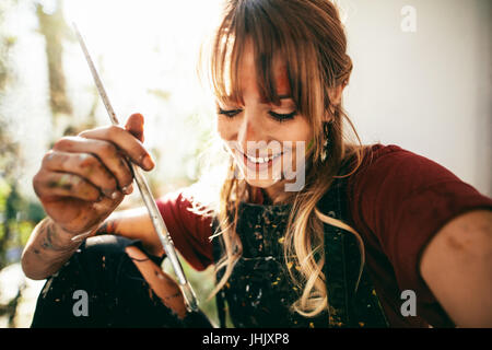 Ravvicinata di una giovane e bella donna caucasica artista con un pennello. Pittore femmina holding spazzola e sorridente. Foto Stock