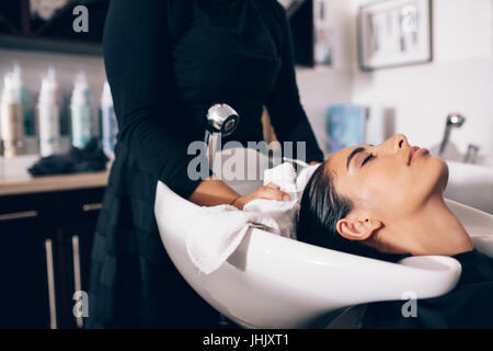 Hair stylist di asciugatura capelli donna con asciugamano in salone. Donna rilassante mentre il parrucchiere si asciuga i capelli bagnati. Foto Stock