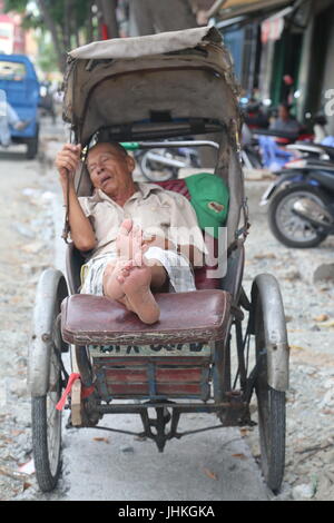 Un maschio il vietnamita in cyclo-rider dorme nel suo ciclo di Ho Chi Minh, Vietnam Foto Stock