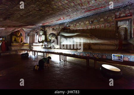 Tempio nella Grotta, SRI LANKA, Marzo 09, 2016 Donna prega in ginocchio di fronte a grandi giacente statua del Buddha Foto Stock