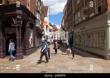 Un occupato la scena dello shopping nella storica città di York in stonegate con una vista della cattedrale di York Minster, sotto un cielo di estate blu Foto Stock