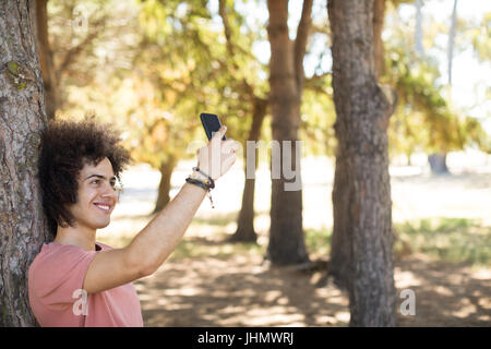 Sorridendo tenendo selfie permanente, mentre di tree tunk al forest Foto Stock