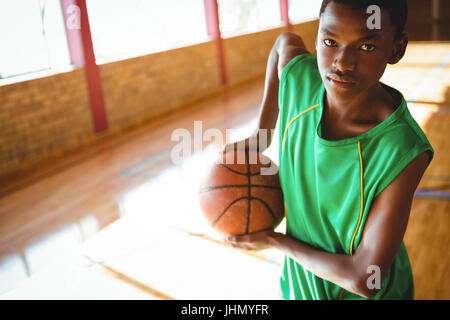 Ritratto di ragazzo adolescente tenendo la pallacanestro mentre in piedi in tribunale Foto Stock