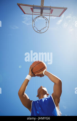 Direttamente sotto al tiro del ragazzo adolescente giocare a basket contro sky sulla giornata di sole Foto Stock