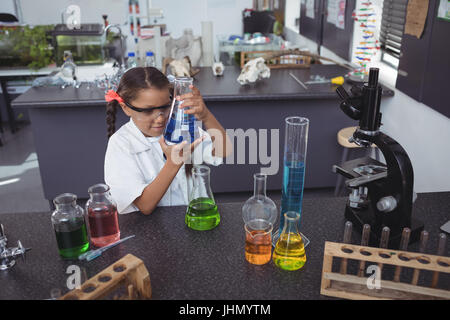 Angolo di alta vista di studente elementare esame chimico blu nel pallone da banco in laboratorio di scienze Foto Stock