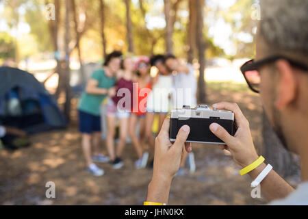 Immagine ritagliata uomo fotografare gli amici mentre si sta in piedi in campeggio Foto Stock