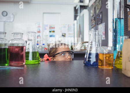 Studente elementare guardando palloni mentre si nasconde dietro la scrivania in Science Laboratory Foto Stock