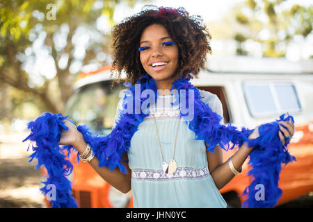 Ritratto di sorridente giovane donna con pelliccia di piume che indossa ciglia artificiali mentre si sta in piedi sul campo Foto Stock