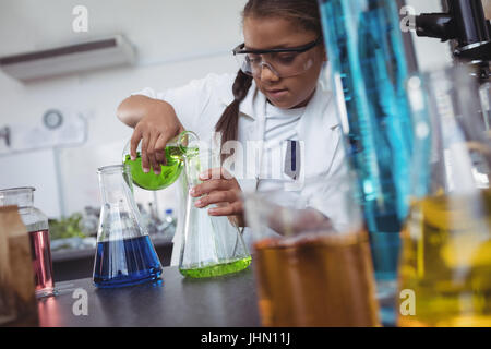 Studente elementare versando chimica verde nel pallone su banco in laboratorio di scienze Foto Stock