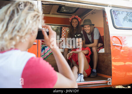 Uomo sorridente fotografare gli amici attraverso la telecamera seduta in camper Foto Stock