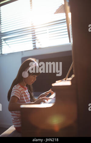 Ragazza di concentrato di indossare le cuffie durante la pratica di pianoforte dal finestrino in aula presso una scuola di musica Foto Stock