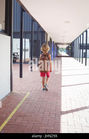 Vista posteriore di scolaro con zaino camminando nel corridoio a scuola sulla giornata di sole Foto Stock