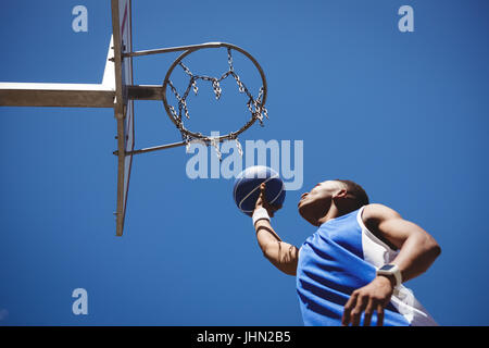 Basso angolo vista del ragazzo adolescente giocare a basket contro il cielo blu chiaro Foto Stock