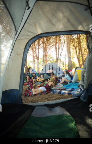 Felice giovani amici godendo insieme sul campo in campeggio visto attraverso la tenda Foto Stock