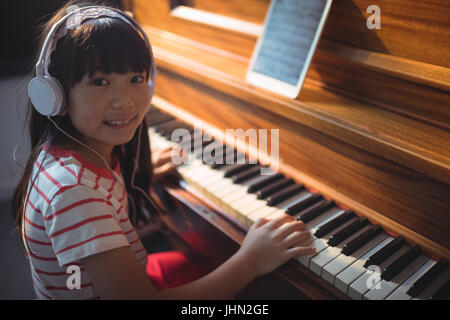 Angolo alto ritratto della ragazza che indossa le cuffie durante la pratica di pianoforte in aula presso una scuola di musica Foto Stock