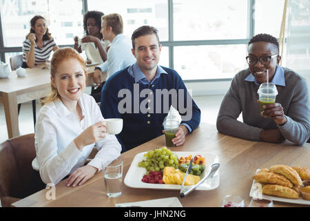 Angolo alto ritratto di sorridere colleghi seduti al tavolo per la colazione in Caffetteria Ufficio Foto Stock