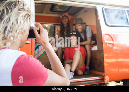 Uomo di fotografare felici amici attraverso la telecamera seduta in camper Foto Stock