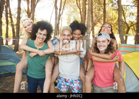 Ritratto di uomini piggybacking amiche mentre si sta in piedi in campeggio Foto Stock