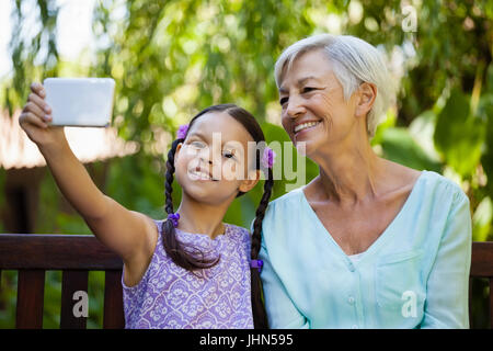 Ragazza sorridente e nonna prendendo selfie in cortile Foto Stock