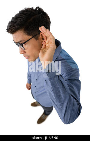 Elevato angolo di visione di imprenditore coppettazione le orecchie mentre in piedi contro uno sfondo bianco Foto Stock
